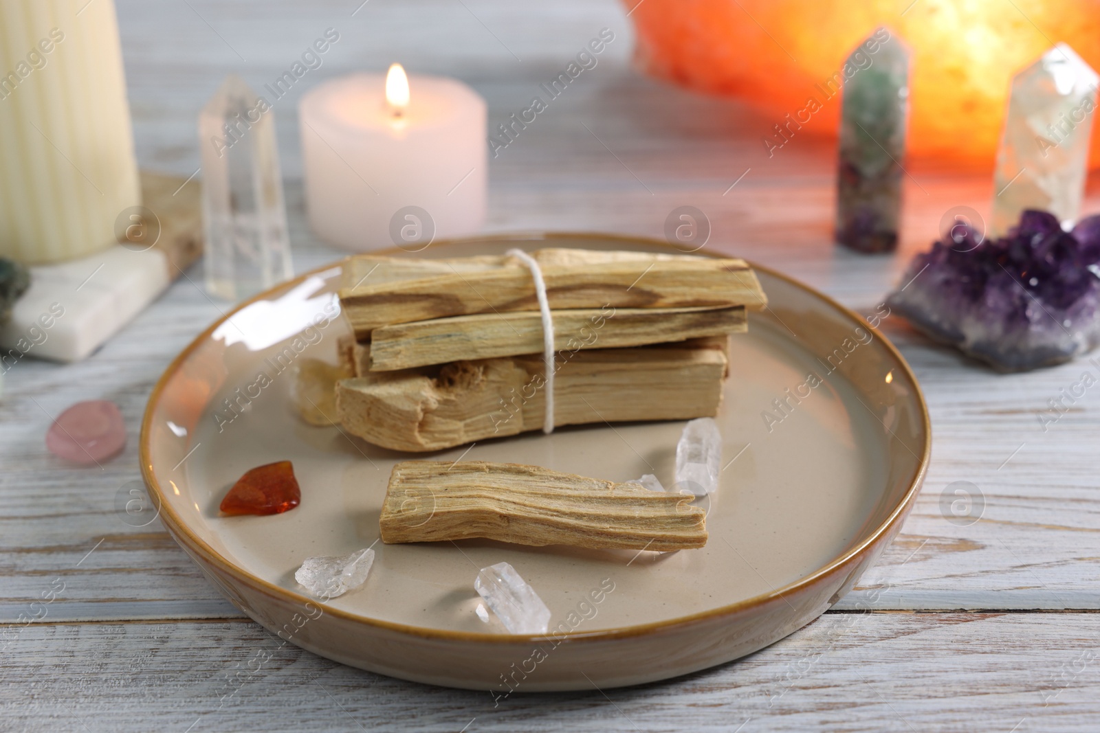 Photo of Palo santo sticks, gemstones and burning candle on white wooden table, closeup