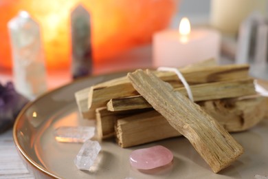 Photo of Palo santo sticks, gemstones and burning candles on white wooden table, closeup