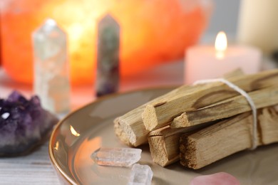 Photo of Palo santo sticks, gemstones and burning candles on white wooden table, closeup