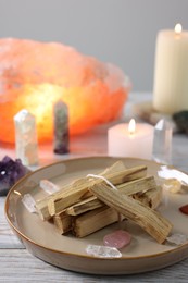 Photo of Palo santo sticks, gemstones and burning candles on white wooden table, closeup