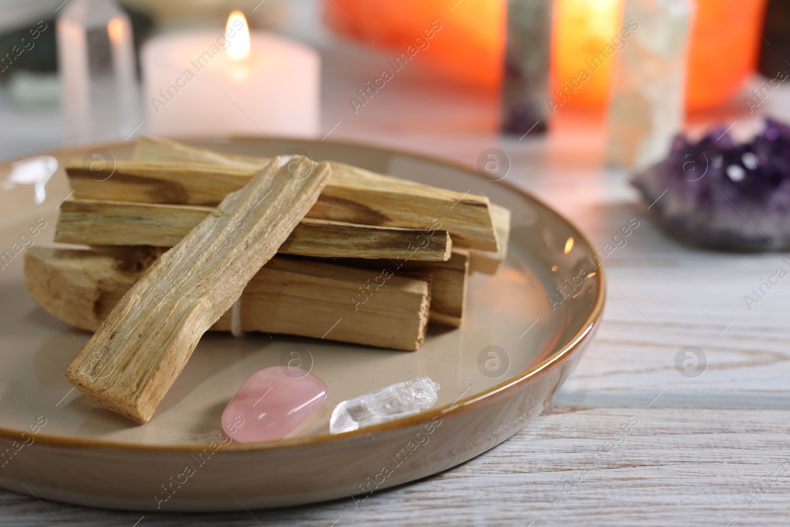 Photo of Palo santo sticks, gemstones and burning candle on white wooden table, closeup