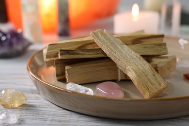 Photo of Palo santo sticks, gemstones and burning candle on white wooden table, closeup