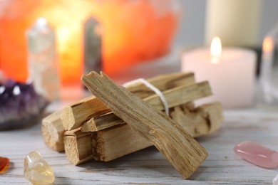 Photo of Palo santo sticks, gemstones and burning candles on white wooden table, closeup