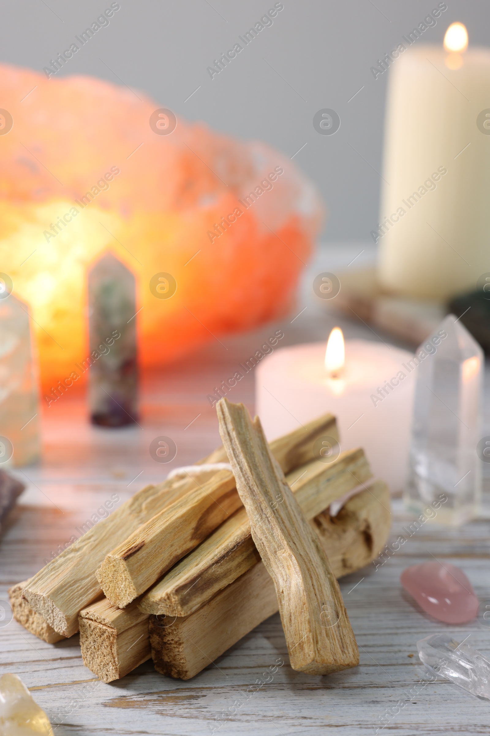 Photo of Palo santo sticks, gemstones and burning candles on white wooden table, closeup