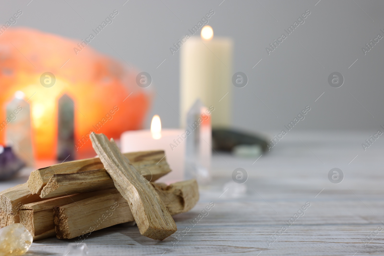 Photo of Palo santo sticks, gemstones and burning candles on white wooden table, closeup