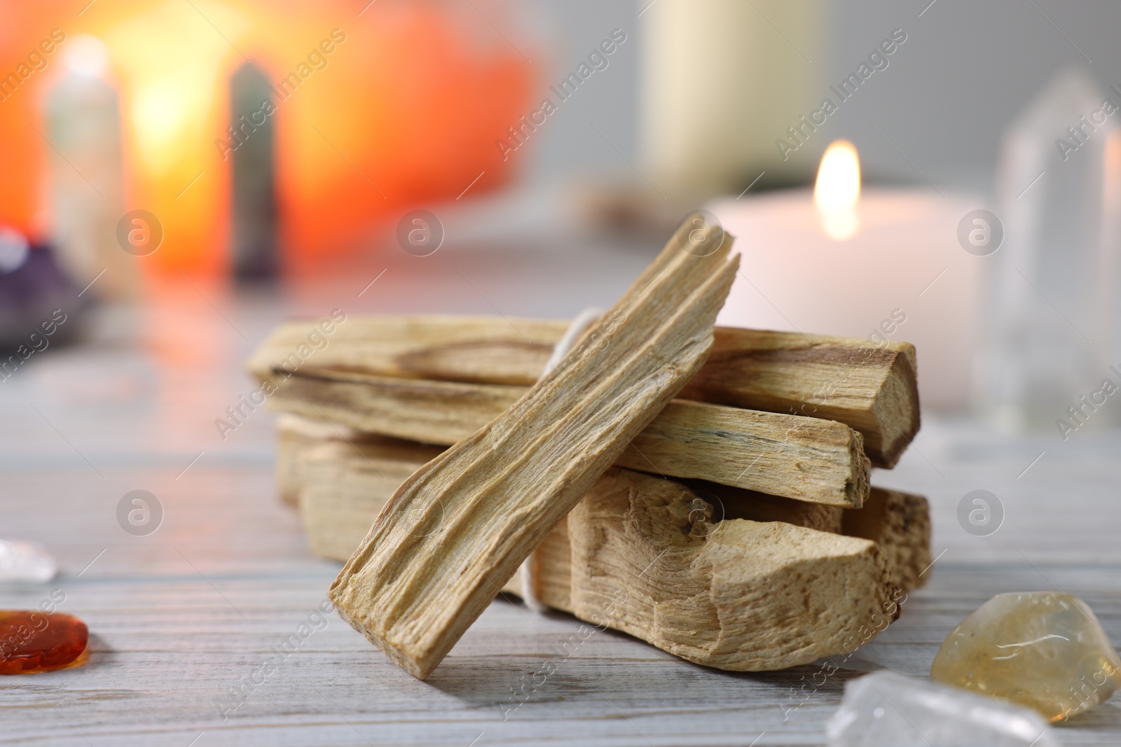 Photo of Palo santo sticks, gemstones and burning candle on white wooden table, closeup