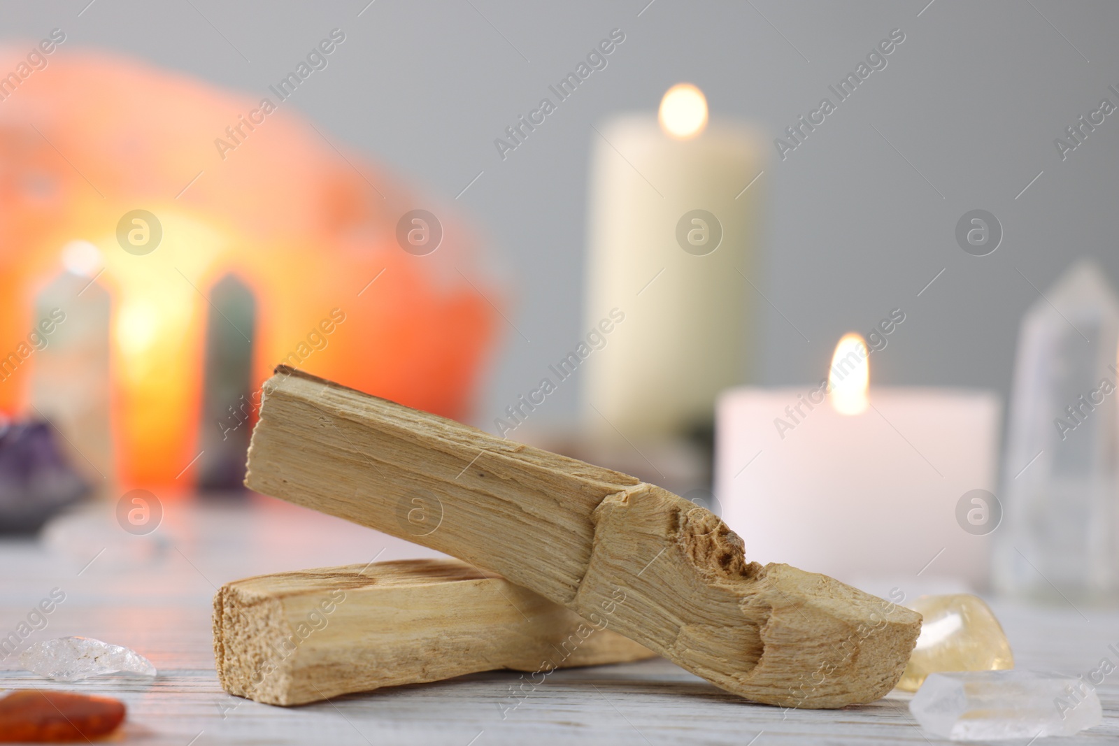 Photo of Palo santo sticks, gemstones and burning candles on white wooden table, closeup