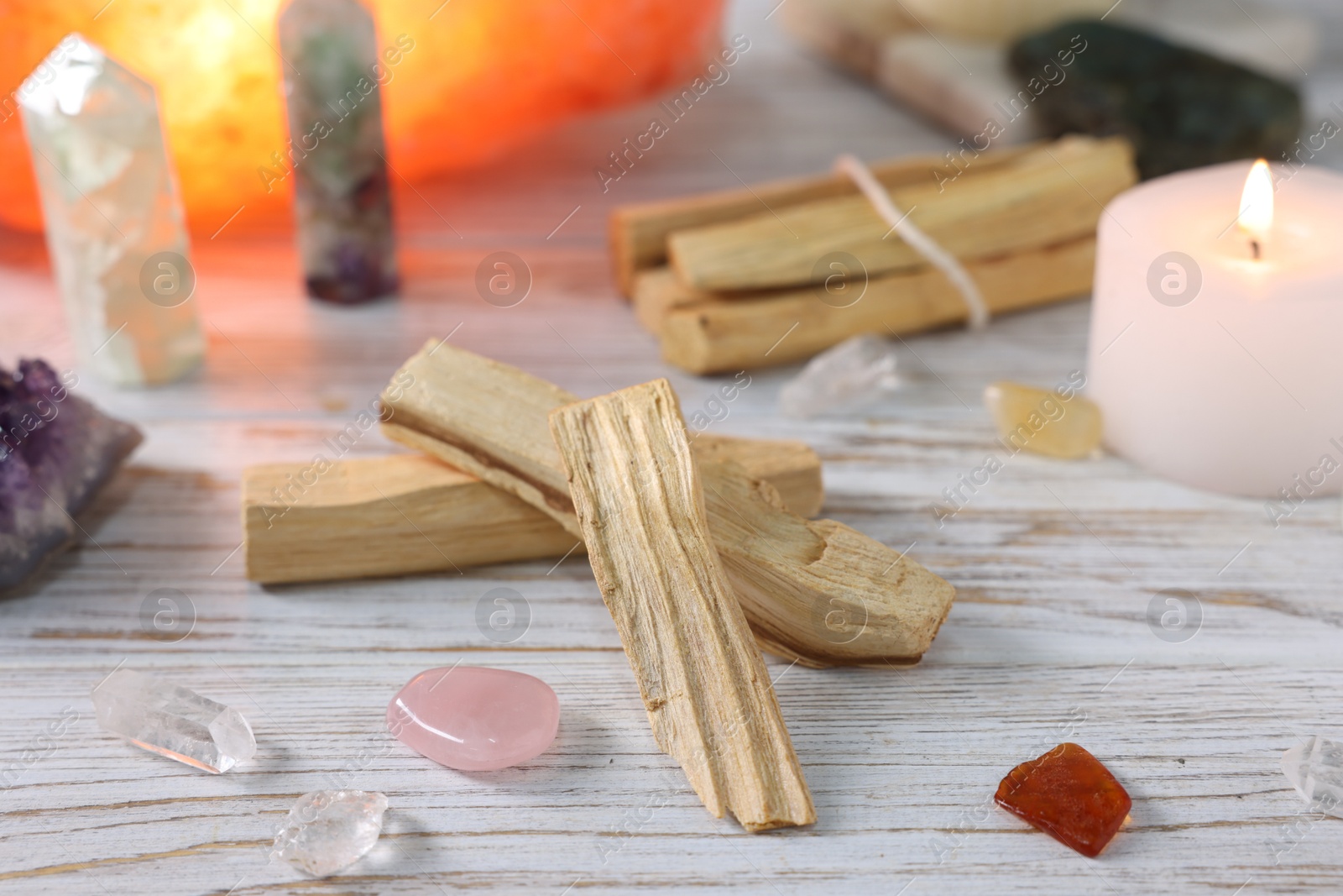 Photo of Palo santo sticks, gemstones and burning candle on white wooden table, closeup