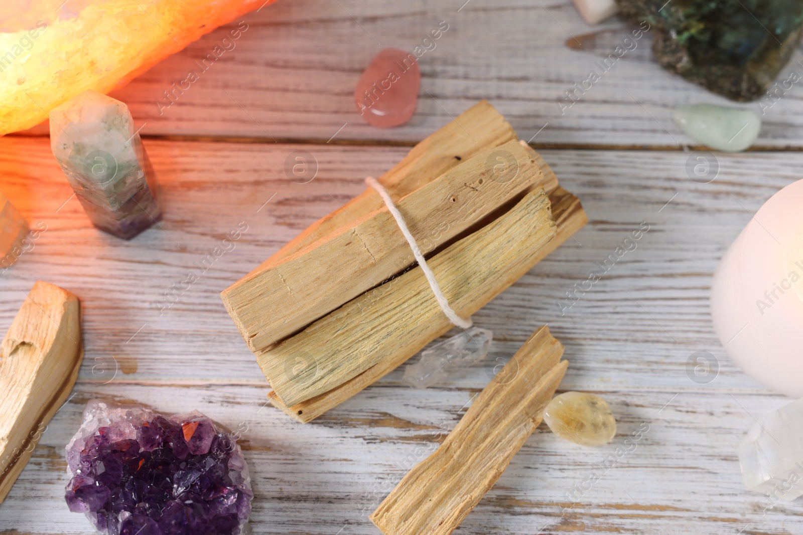 Photo of Palo santo sticks, gemstones and candle on white wooden table, flat lay