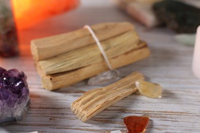 Photo of Palo santo sticks and gemstones on white wooden table, closeup