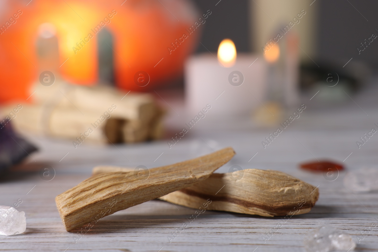 Photo of Palo santo sticks, gemstones and burning candle on white wooden table, closeup