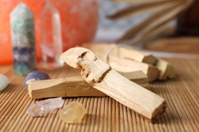 Photo of Palo santo sticks and gemstones on bamboo mat, closeup