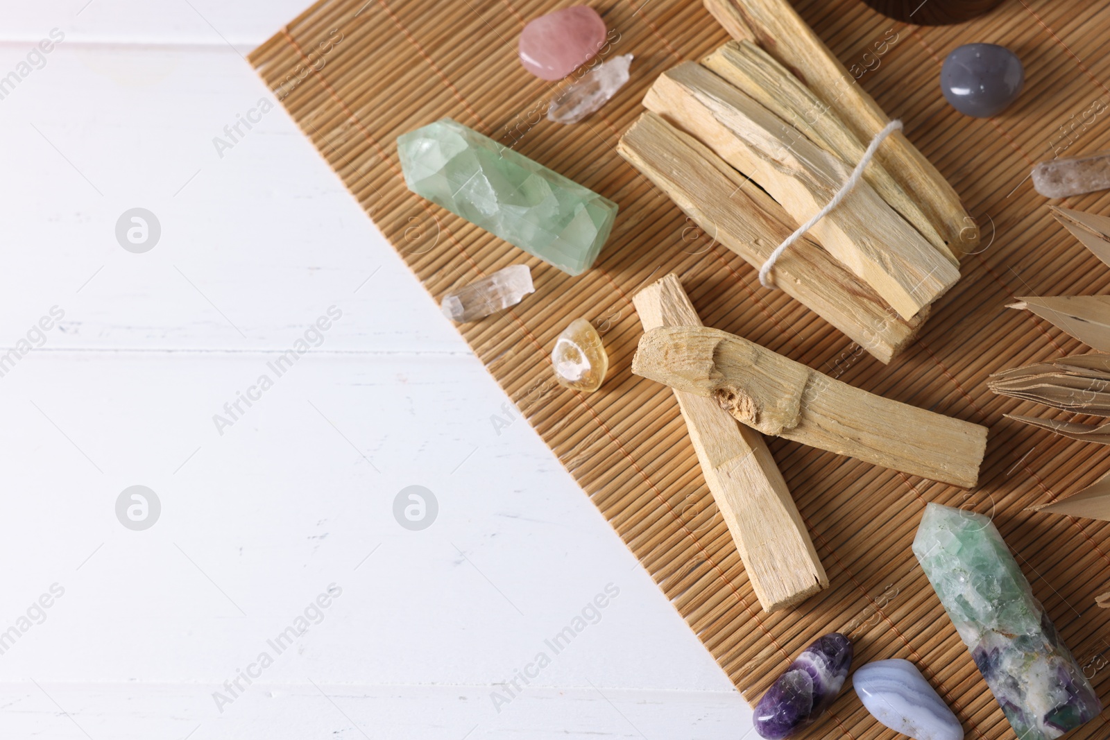 Photo of Palo santo sticks and gemstones on white wooden table, flat lay. Space for text