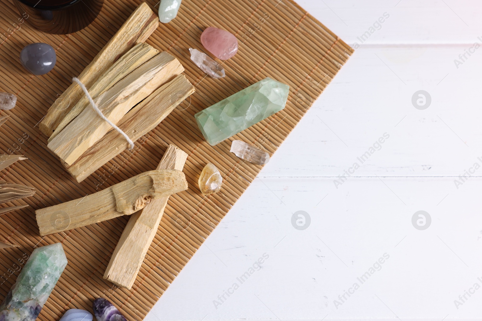 Photo of Palo santo sticks and gemstones on white wooden table, flat lay. Space for text