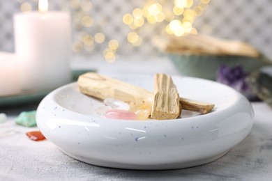 Photo of Palo santo sticks, gemstones and burning candle on light grey textured table, closeup