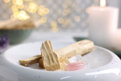 Photo of Palo santo sticks, gemstones and burning candle on table, closeup