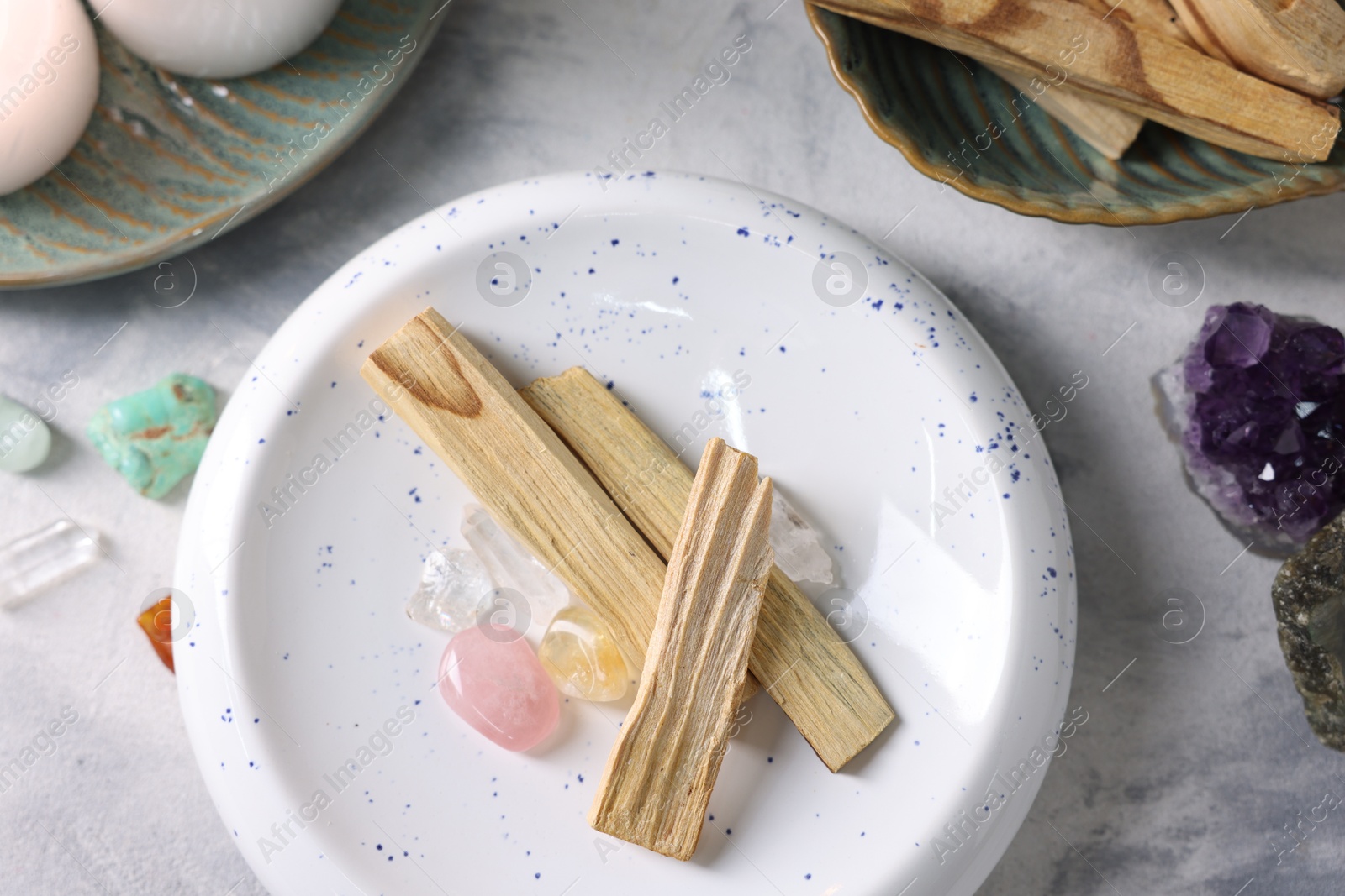 Photo of Palo santo sticks and gemstones on light grey textured table, flat lay