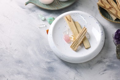 Photo of Palo santo sticks and gemstones on light grey textured table, flat lay. Space for text