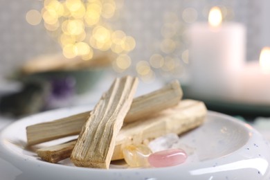 Photo of Palo santo sticks, gemstones and burning candles on table, closeup