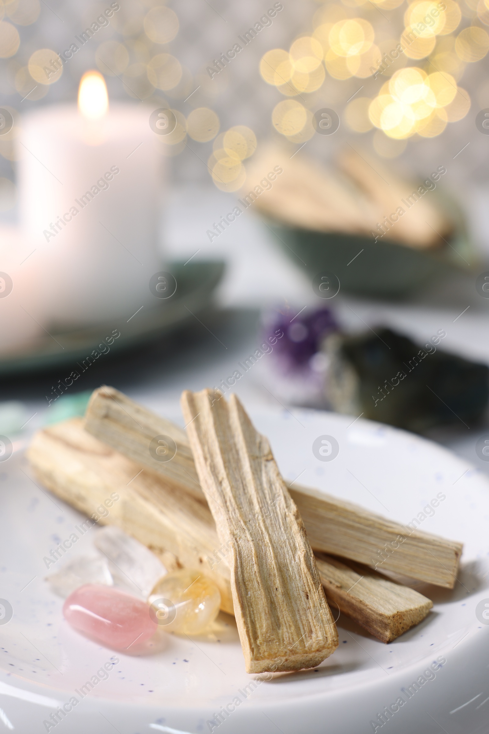 Photo of Palo santo sticks, gemstones and burning candle on table, closeup