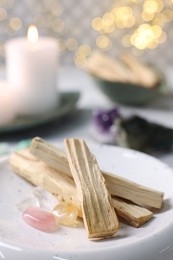 Photo of Palo santo sticks, gemstones and burning candle on table, closeup