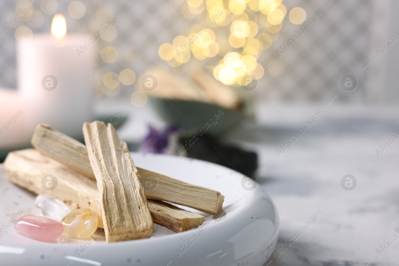 Photo of Palo santo sticks, gemstones and burning candle on light grey table, closeup. Space for text