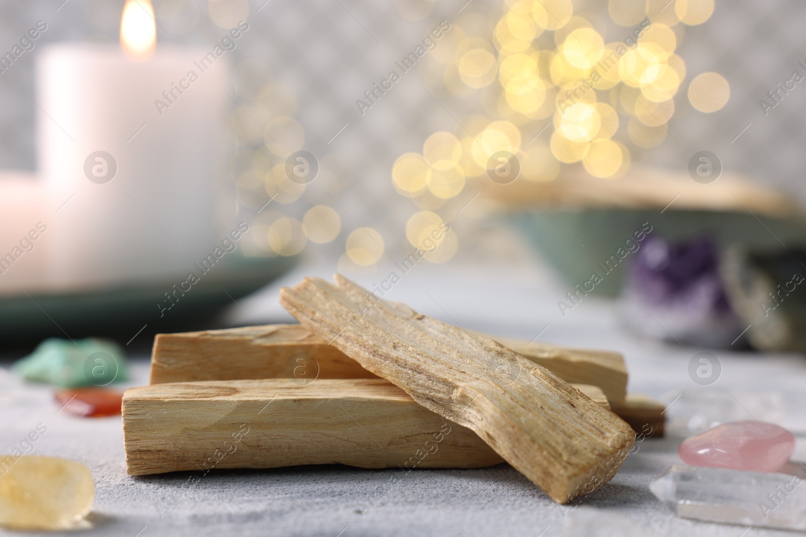 Photo of Palo santo sticks, gemstones and burning candle on light grey textured table, closeup