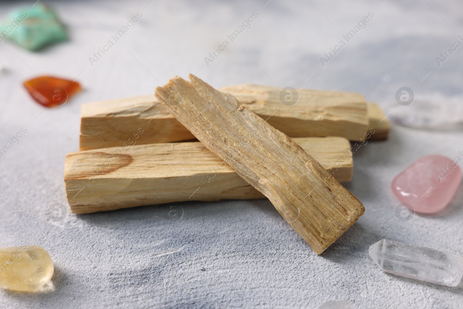 Photo of Palo santo sticks and gemstones on light grey textured table, closeup