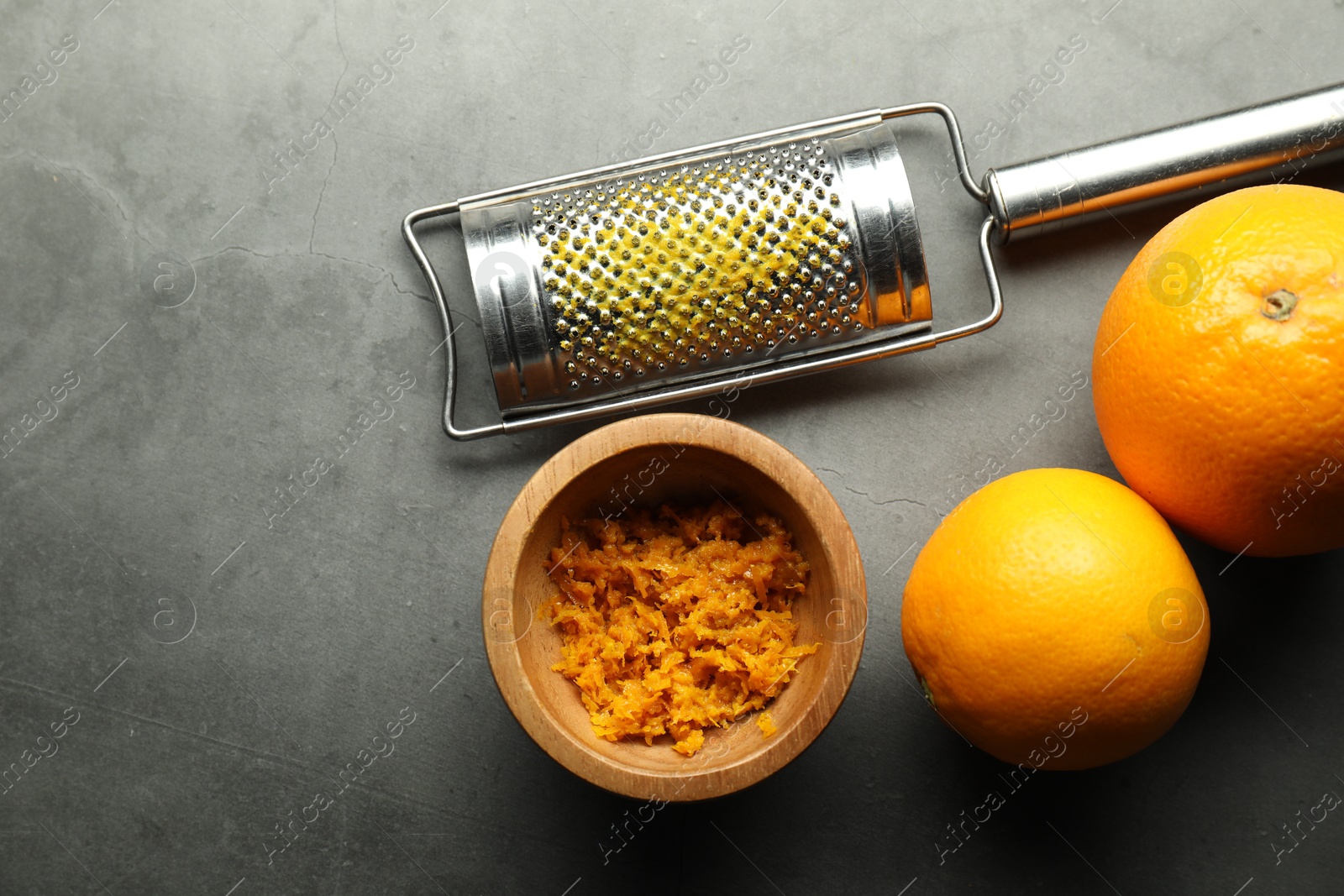 Photo of Orange zest, grater and fresh fruits on gray textured table, flat lay. Space for text