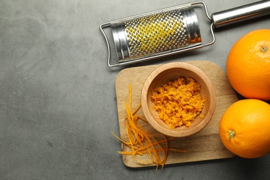 Photo of Orange zest, grater and fresh fruits on gray textured table, flat lay. Space for text