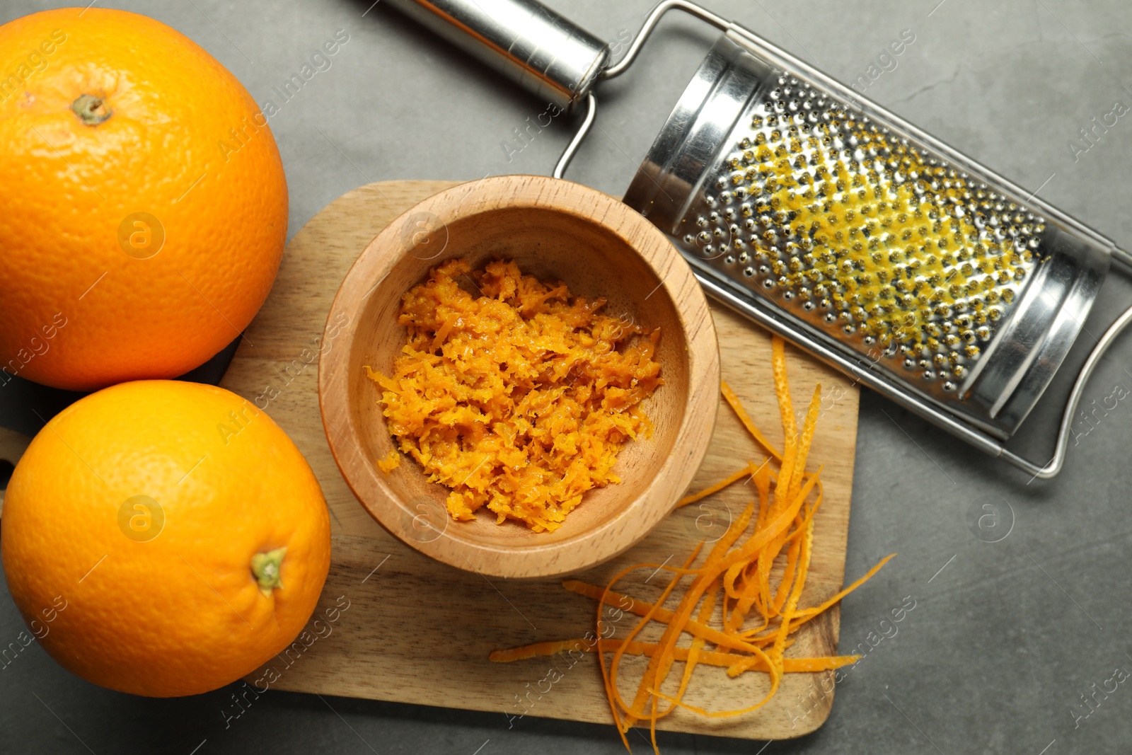 Photo of Orange zest, grater and fresh fruits on gray textured table, flat lay