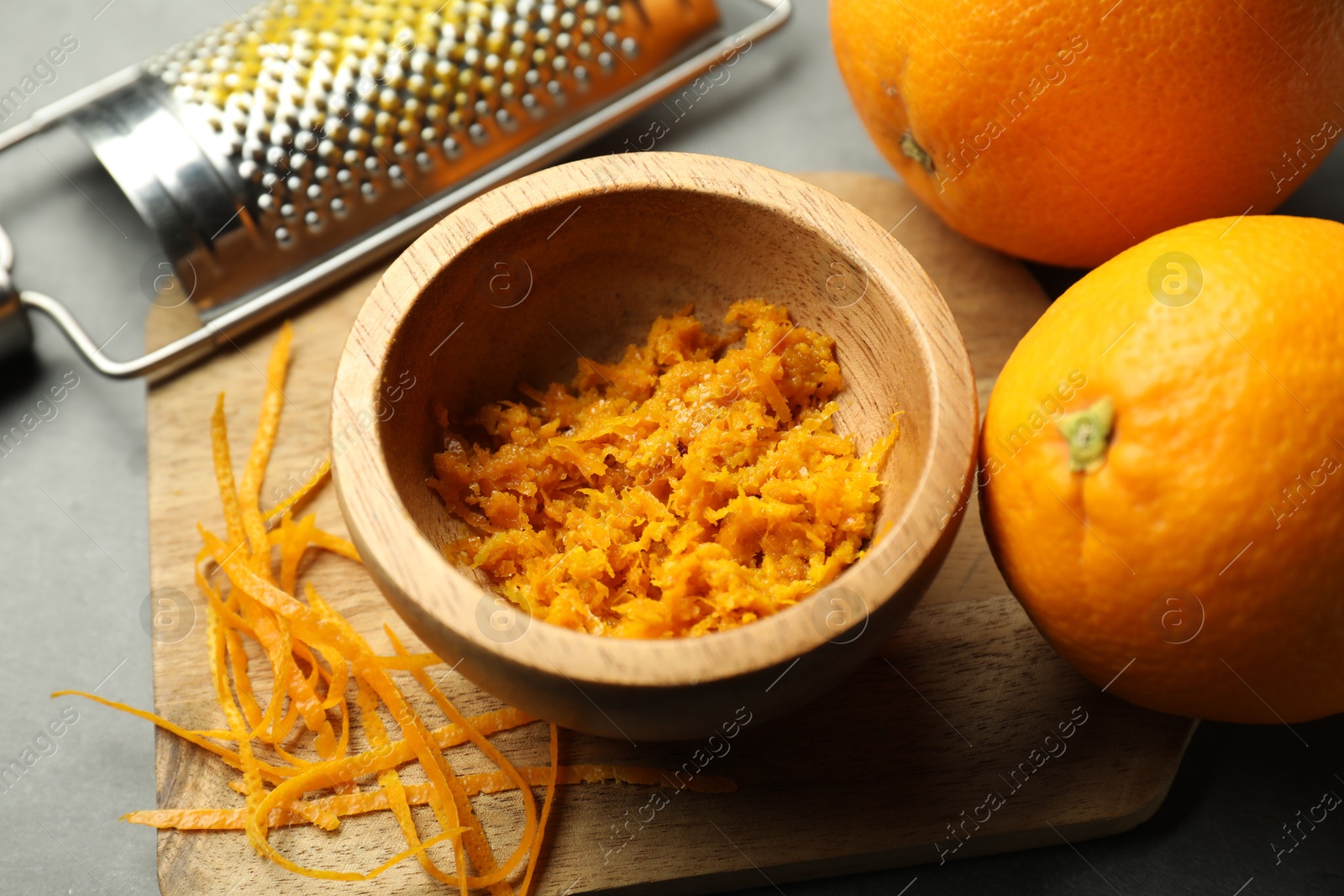 Photo of Orange zest, grater and fresh fruits on gray table, closeup