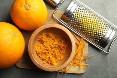 Photo of Orange zest, grater and fresh fruits on gray textured table, flat lay