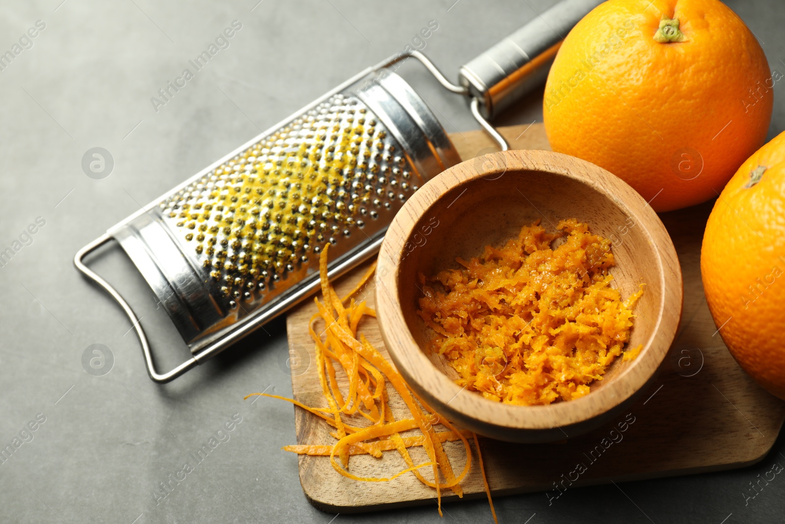 Photo of Orange zest, grater and fresh fruits on gray textured table, closeup