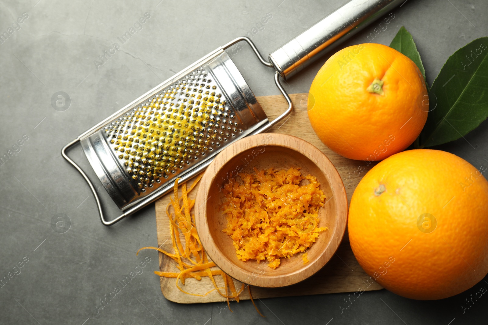 Photo of Orange zest, grater and fresh fruits on gray textured table, flat lay