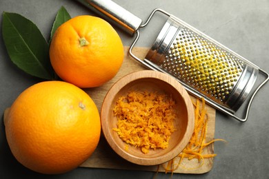 Photo of Orange zest, grater and fresh fruits on gray textured table, flat lay