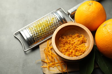 Photo of Orange zest, grater and fresh fruits on gray textured table, closeup