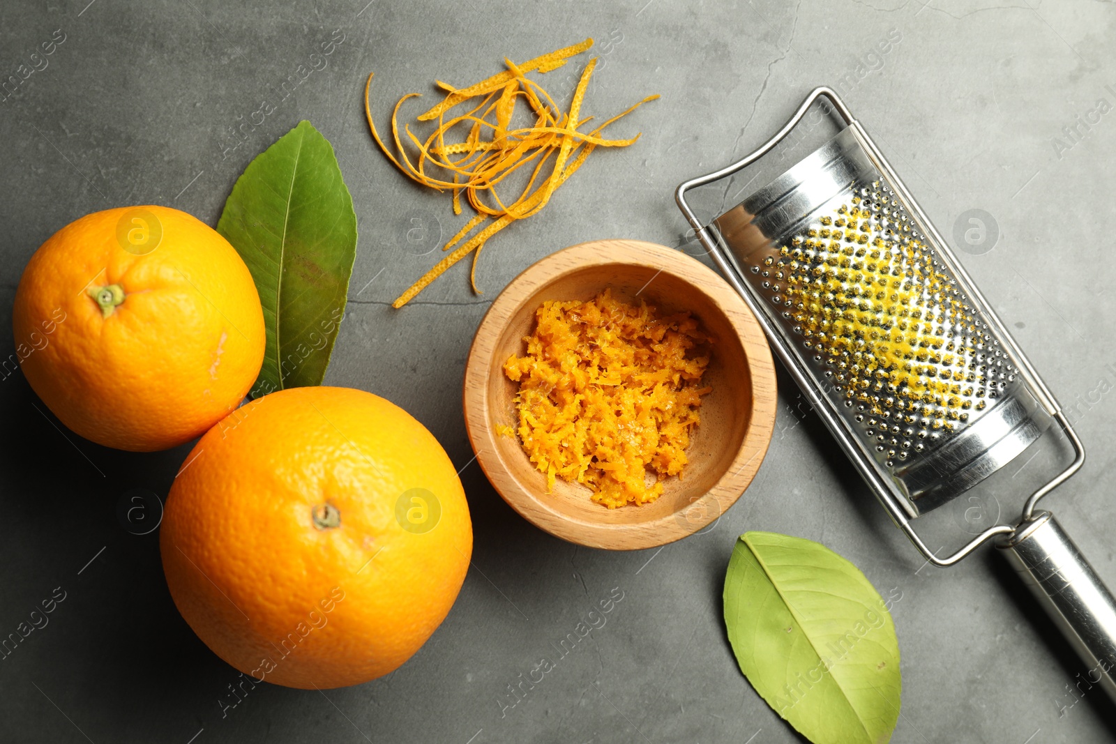 Photo of Orange zest, grater and fresh fruits on gray textured table, flat lay