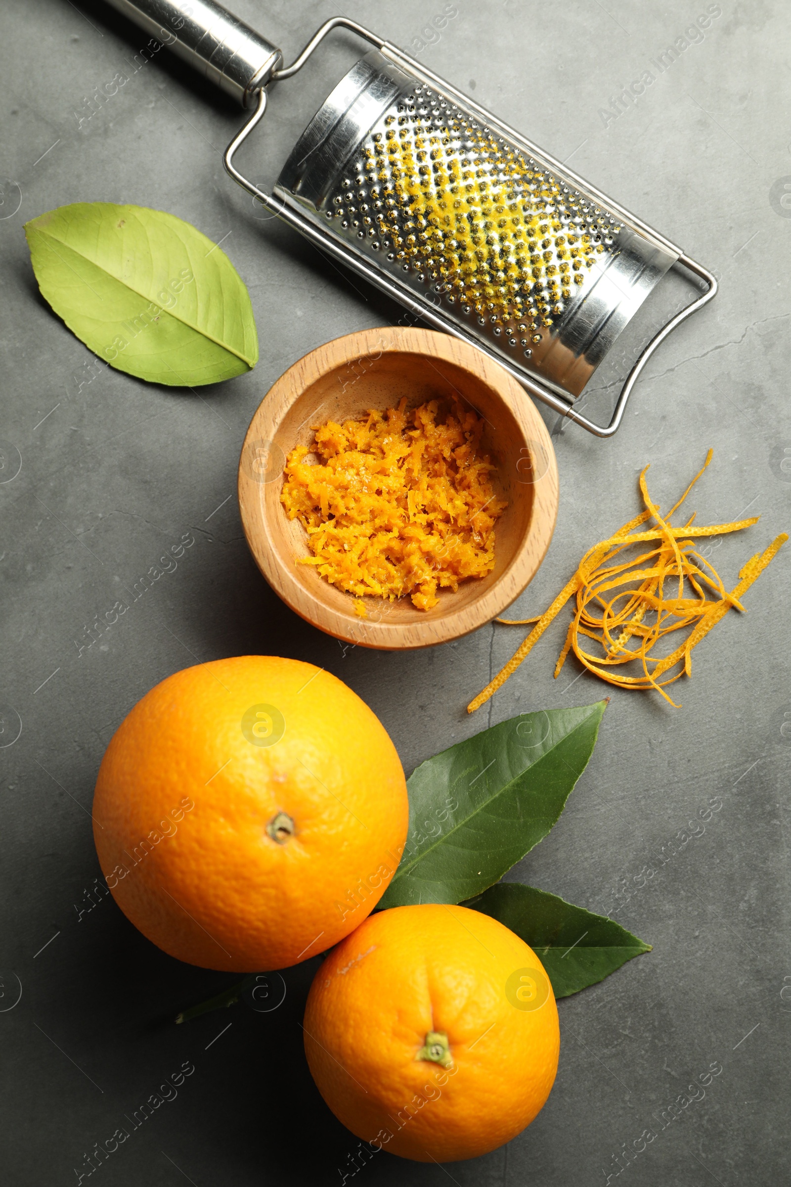 Photo of Orange zest, grater and fresh fruits on gray textured table, flat lay