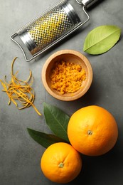 Photo of Orange zest, grater and fresh fruits on gray textured table, flat lay