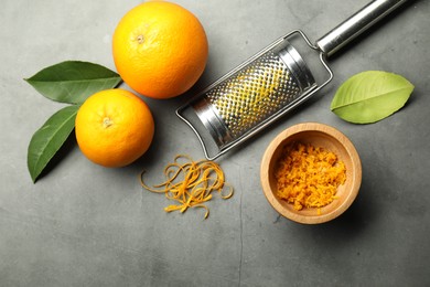 Photo of Orange zest, grater and fresh fruits on gray textured table, flat lay. Space for text