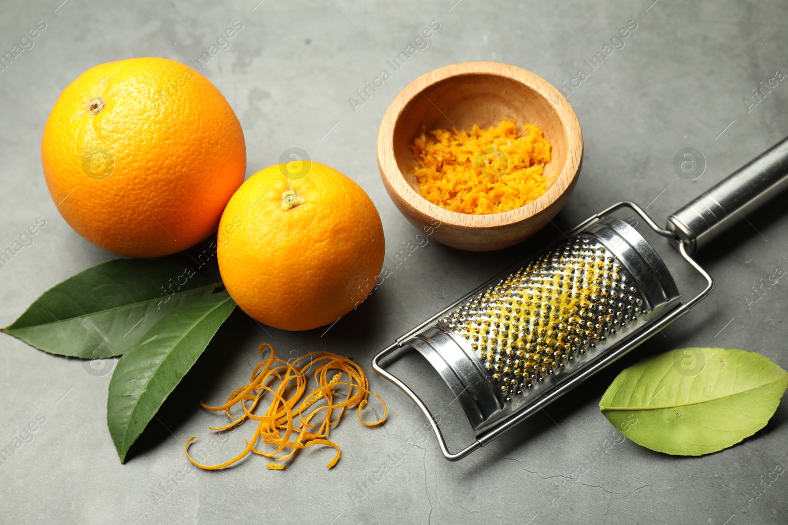 Photo of Orange zest, grater and fresh fruits on gray textured table