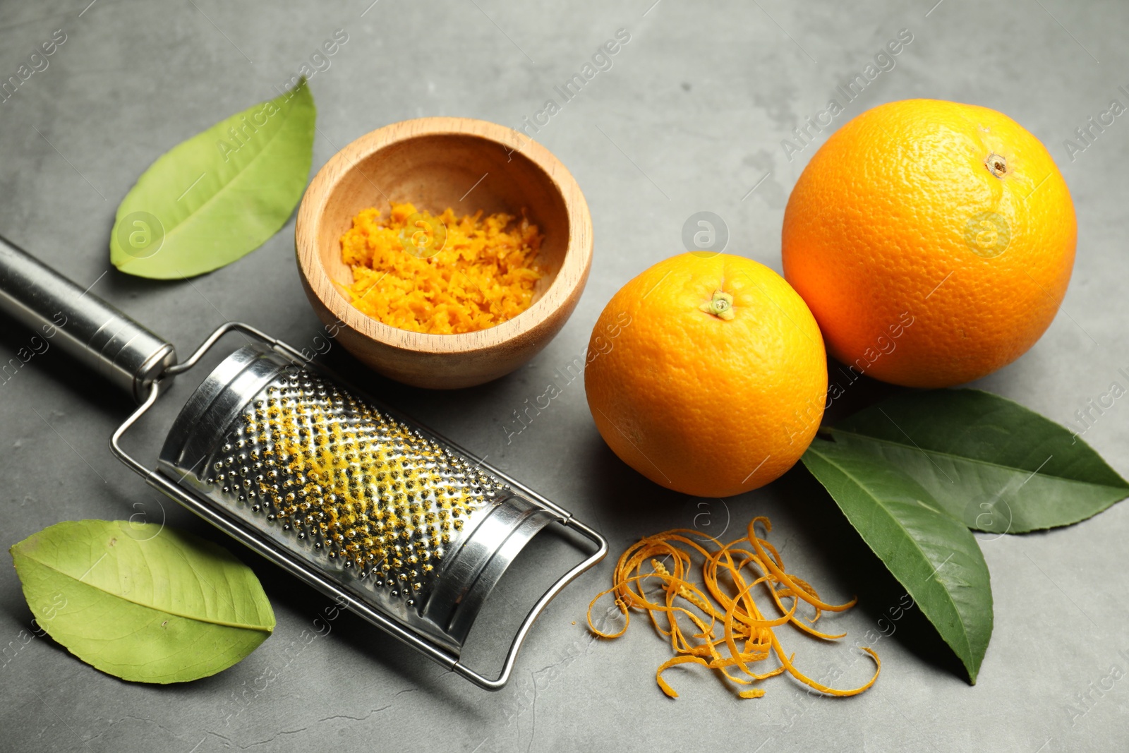 Photo of Orange zest, grater and fresh fruits on gray textured table