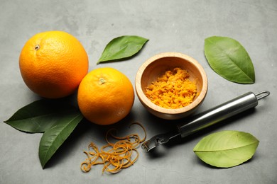 Photo of Orange zest, zester tool and fresh fruits on gray textured table