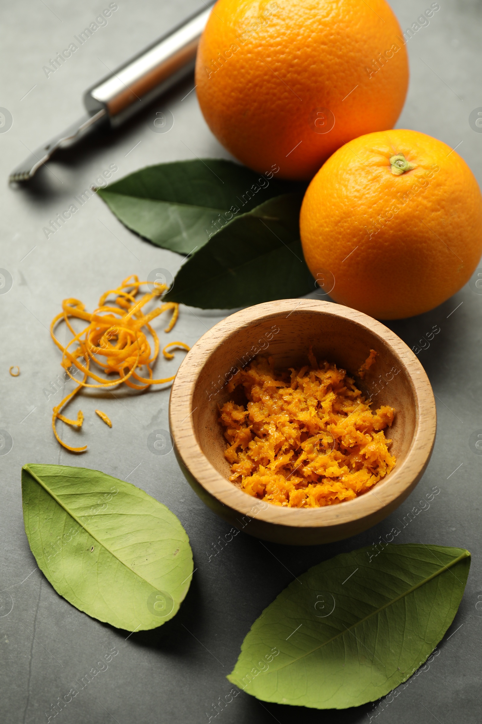 Photo of Orange zest, zester tool and fresh fruits on gray textured table, flat lay