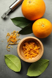 Photo of Orange zest, zester tool and fresh fruits on gray textured table, flat lay