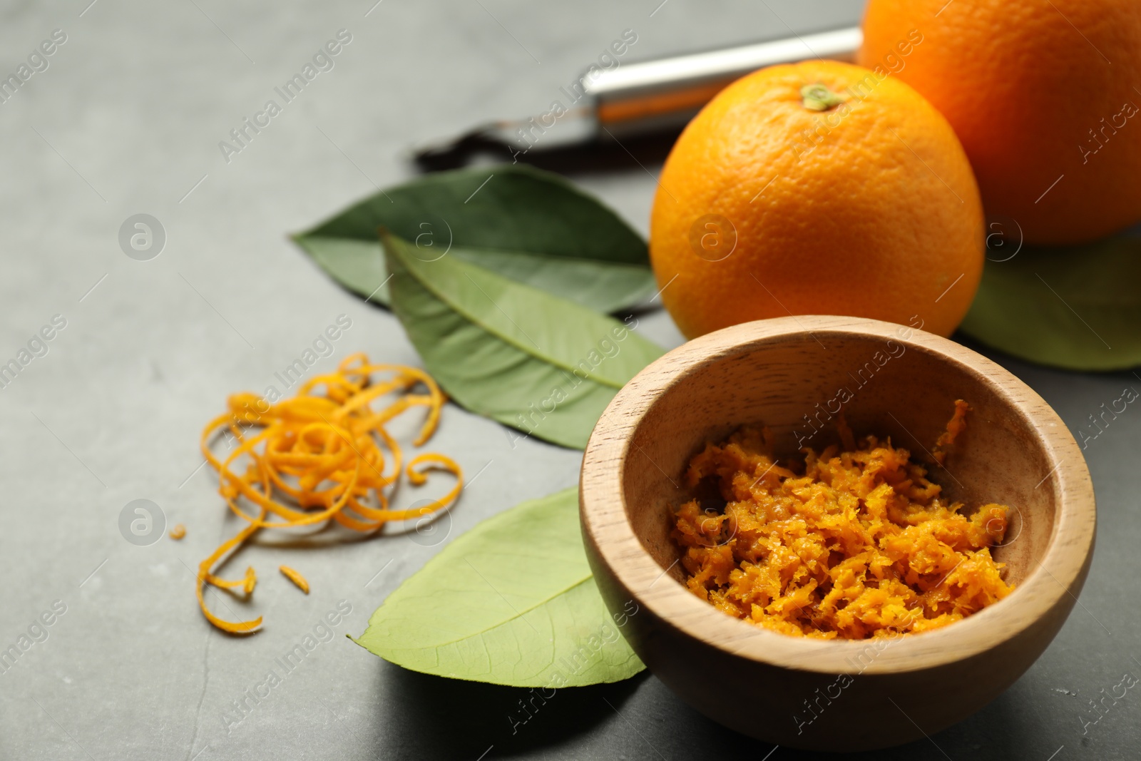 Photo of Orange zest in bowl and fresh fruits on gray textured table, closeup. Space for text