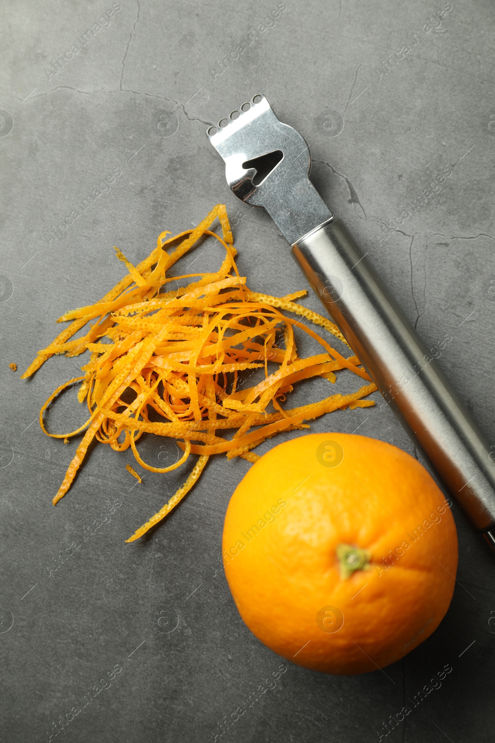 Photo of Orange zest, zester tool and fresh fruit on gray textured table, flat lay