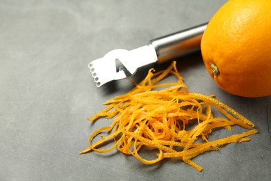 Photo of Orange zest, zester tool and fresh fruit on gray textured table, closeup. Space for text