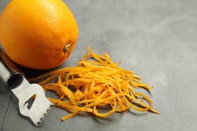 Photo of Orange zest, zester tool and fresh fruit on gray textured table, closeup. Space for text